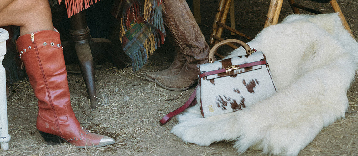 Three women in cowboy hats sitting at a table with cowboy boots and a handbag in a rustic setting.